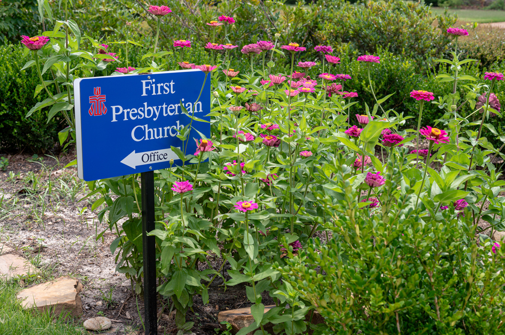 Sign reading "First Presbyterian Church" surrounded by pink flowers.
