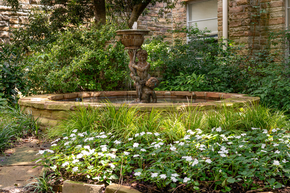 A fountain surrounded by shrubs and white flowers.