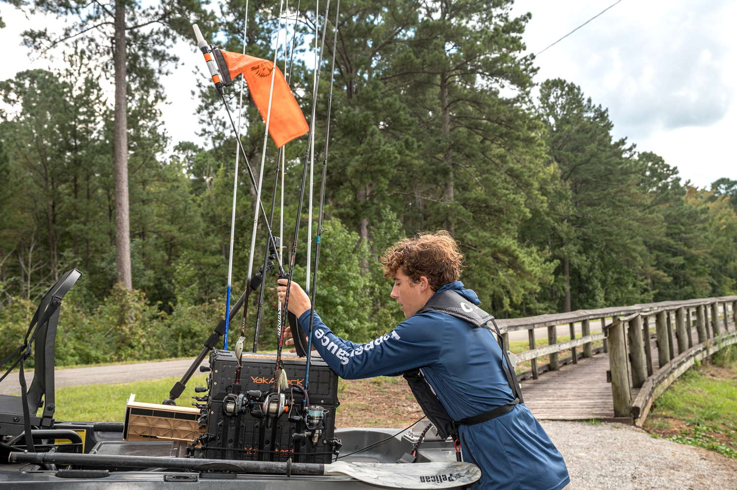 A young person adjusts fishing rods on a kayak.