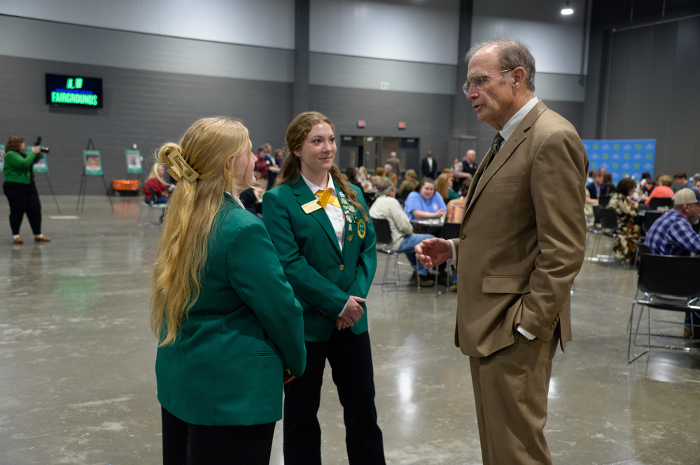 Two teens in green jackets talk to a man wearing a suit and gesturing.