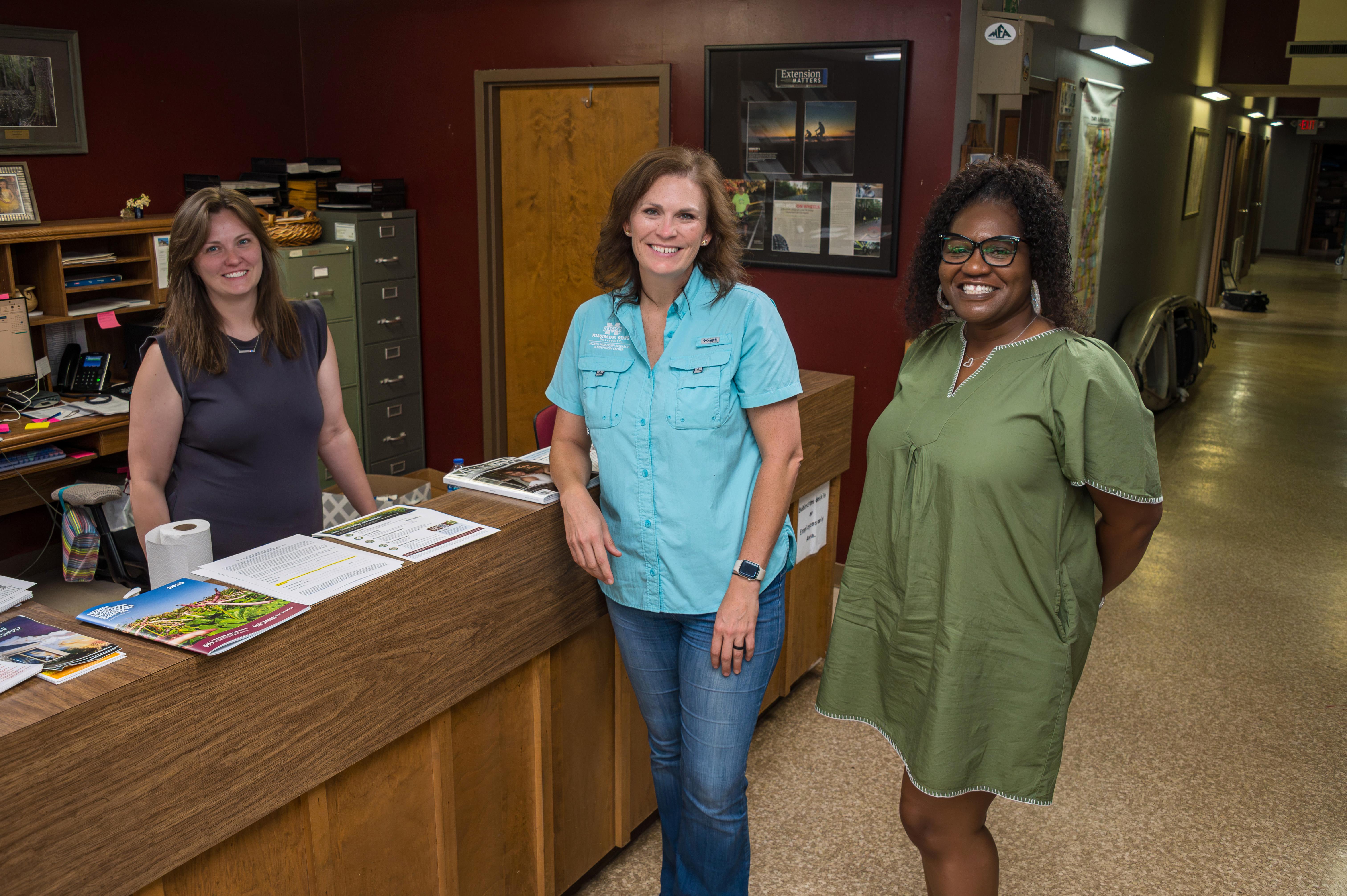 Three people standing and smiling in an office.