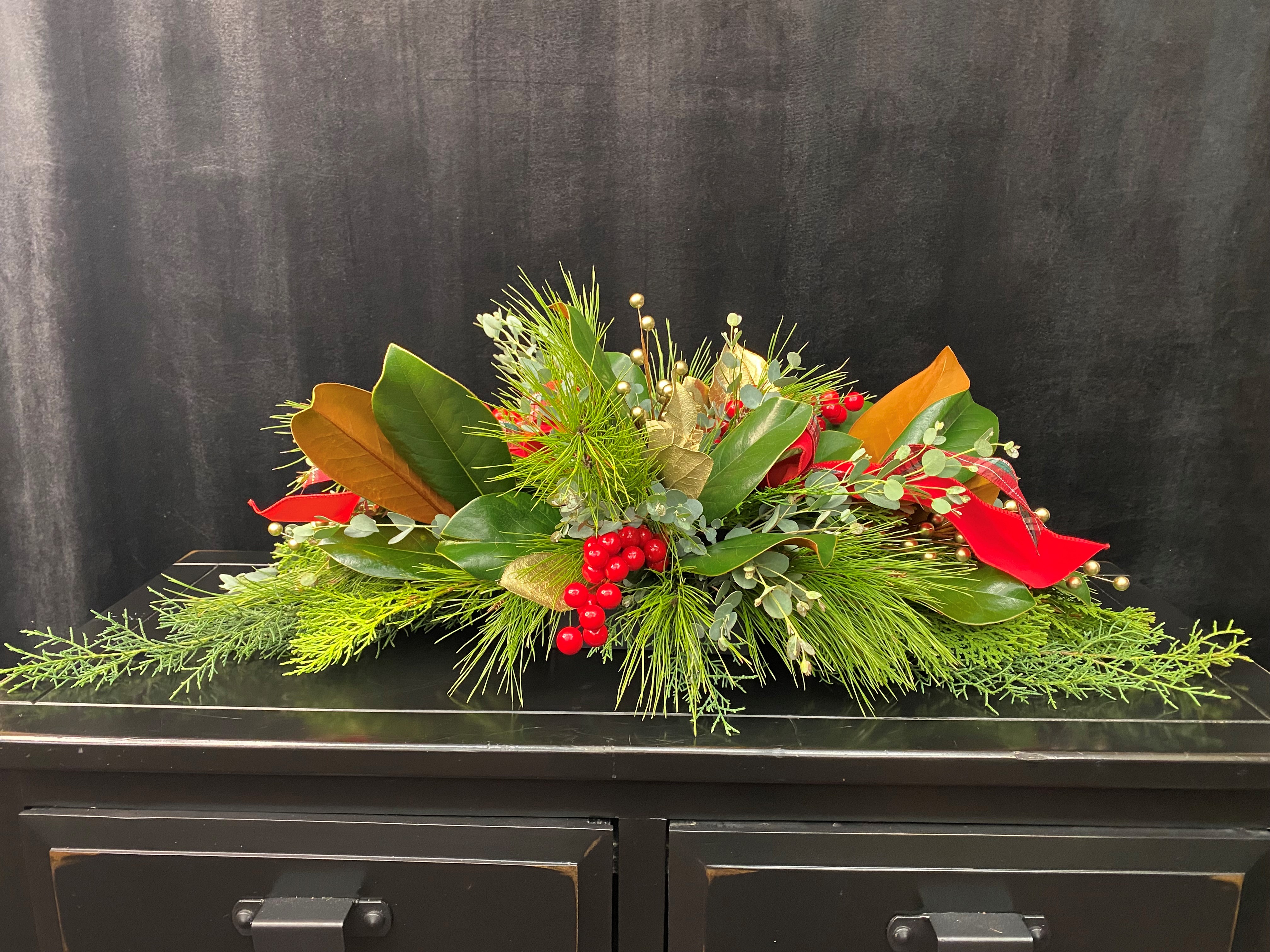 A christmas floral arrangement with various greenery and red berries.