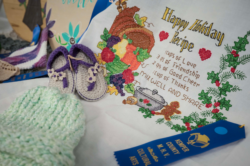 An assortment of homemade crafts, including baby booties, a tobaggan, and embroidery.