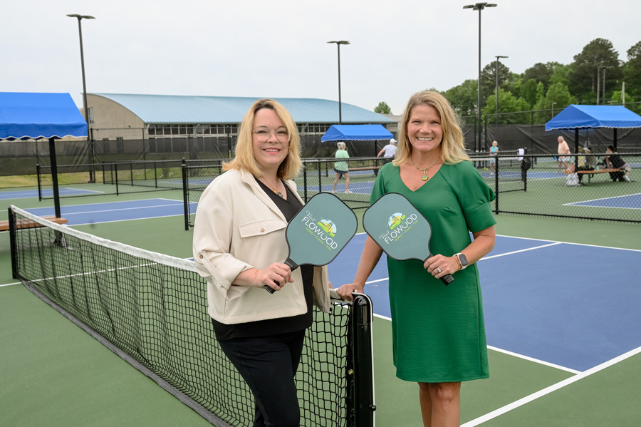 Two smiling people holding paddles stand on a pickleball court. 