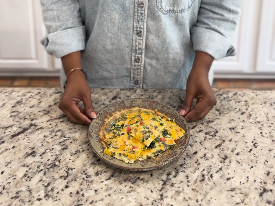 A woman stands at a kitchen counter with a plate of Sheet Pan Eggs and Veggies.