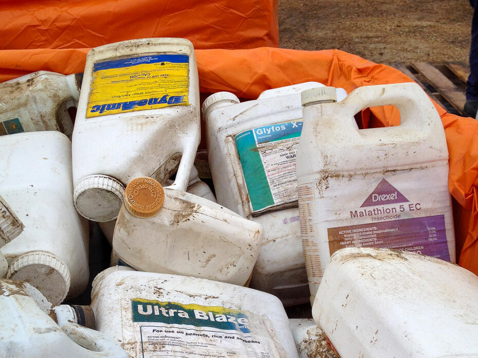 Pile of used agricultural chemical containers in an orange-lined bin.