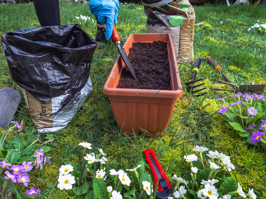 Woman mixing potting soil with a trowel in a pot on a lawn.