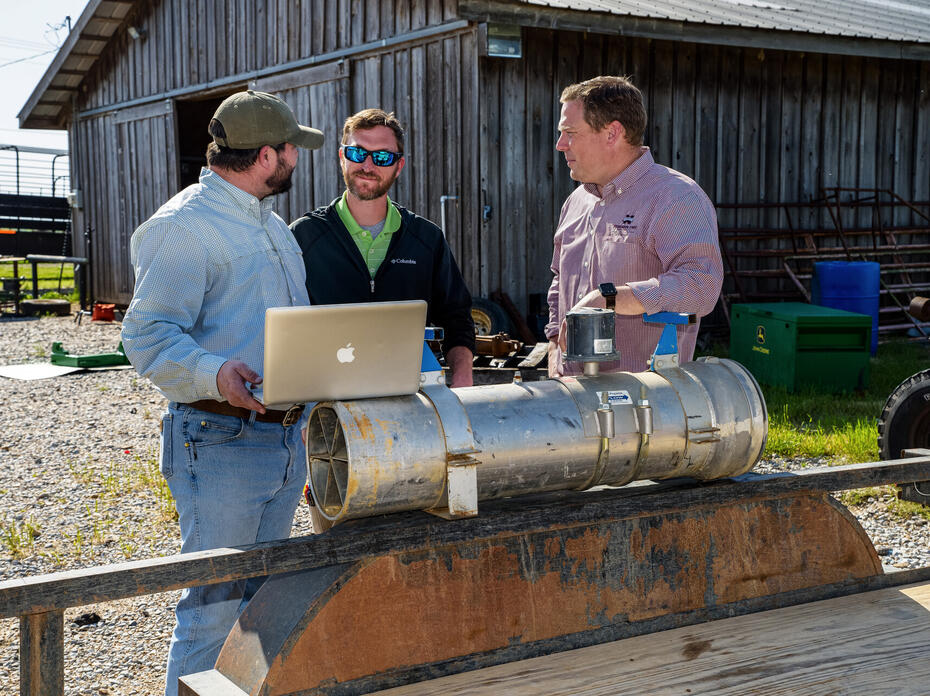 Three men stand around a trailer that holds a large irrigation pipe.