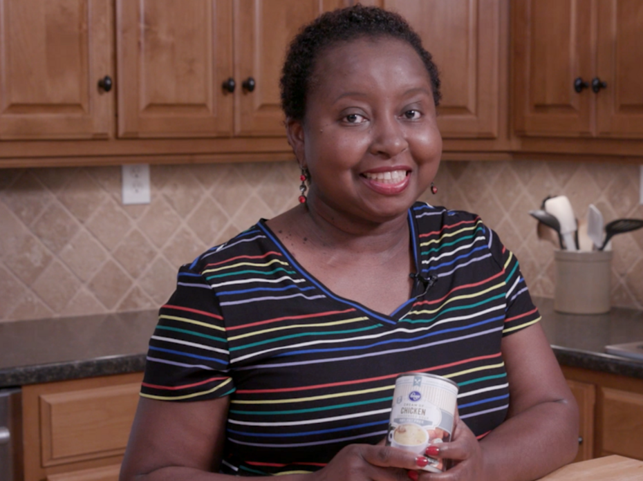 A woman stands in a kitchen while holding a can of reduced fat cream of chicken soup. 