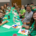 Teens smiling with an adult at a table full of painting supplies.