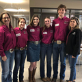 Six people, including two women, three girls, and one boy, wearing maroon polo shirts and smiling at the camera.