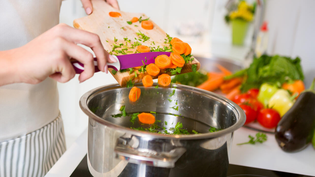 Person dumping vegetables in a pot.