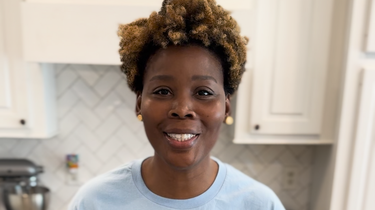 A woman stands in a kitchen with ingredients for a yogurt parfait on the counter.