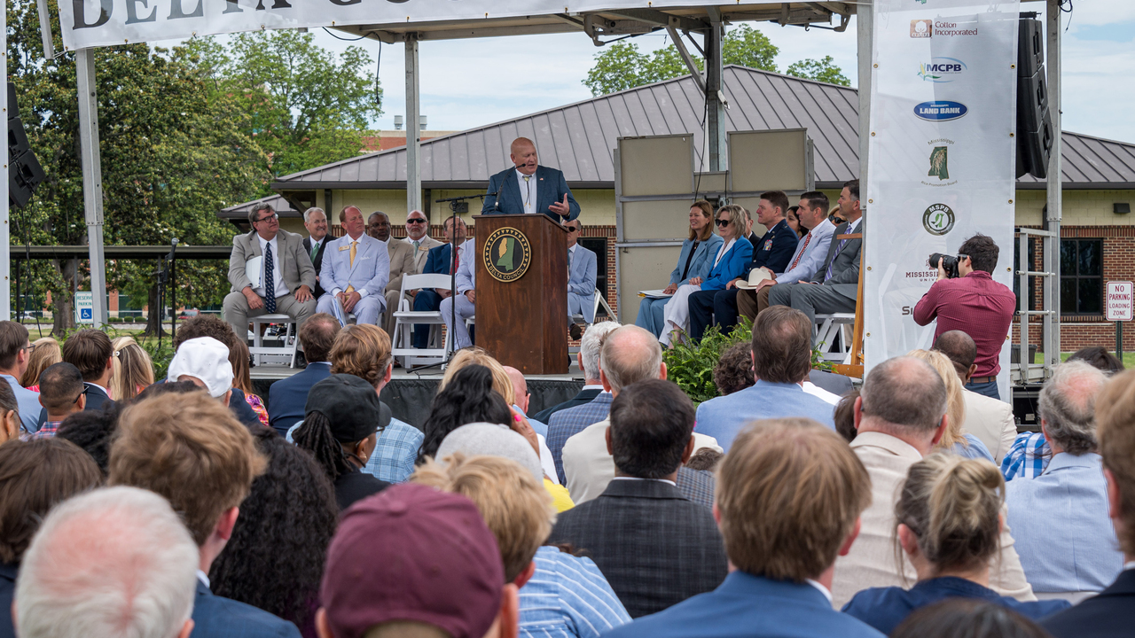 A man speaks to a large crowd from an outdoor stage.