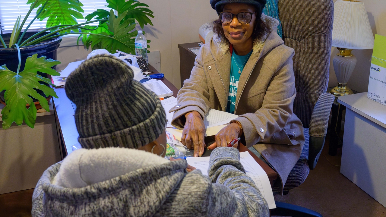 Two women face each other over a desk to review paperwork. 
