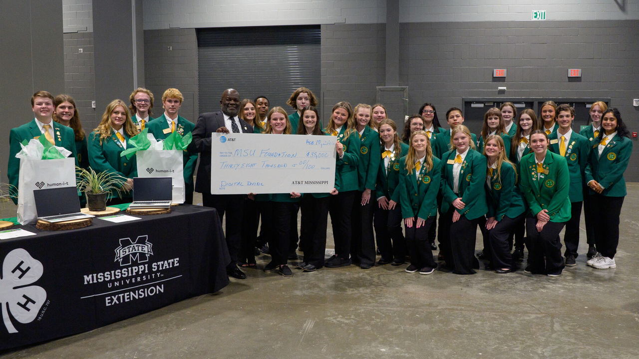 A large group of teenagers pose for a photo with a man holding a large presentation-style check.