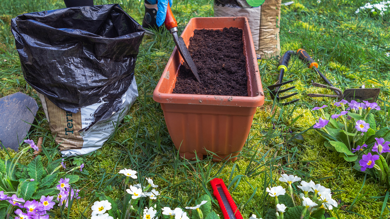 Woman mixing potting soil with a trowel in a pot on a lawn.