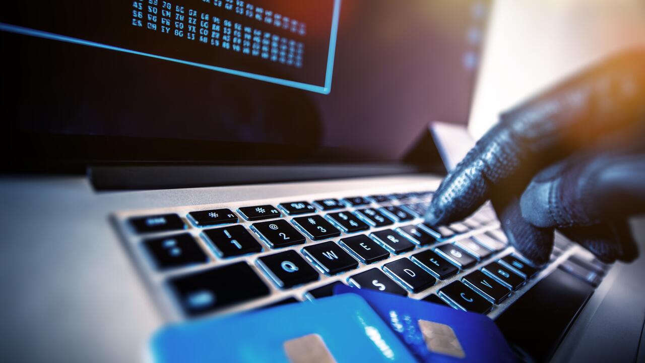 Person with gloves types in credit card number on computer.