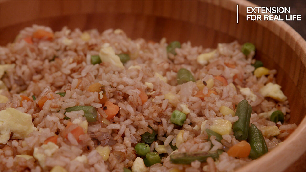 A brown bamboo bowl filled with fried rice made with brown rice, scrambled egg, and mixed vegetables including green beans, peas, carrots and corn. 