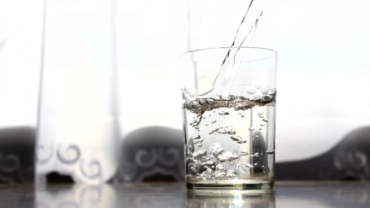 A person off-camera pours water into a glass.