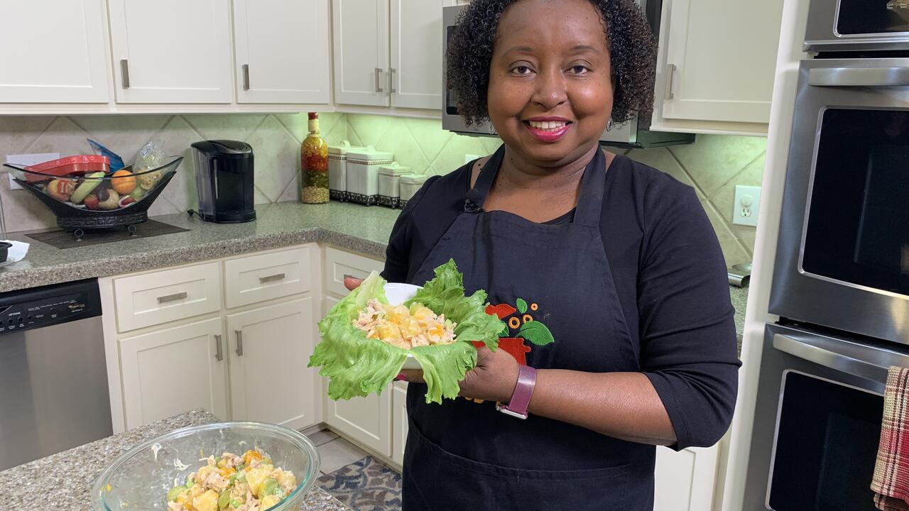A woman holds a bowl of chicken and fruit salad.