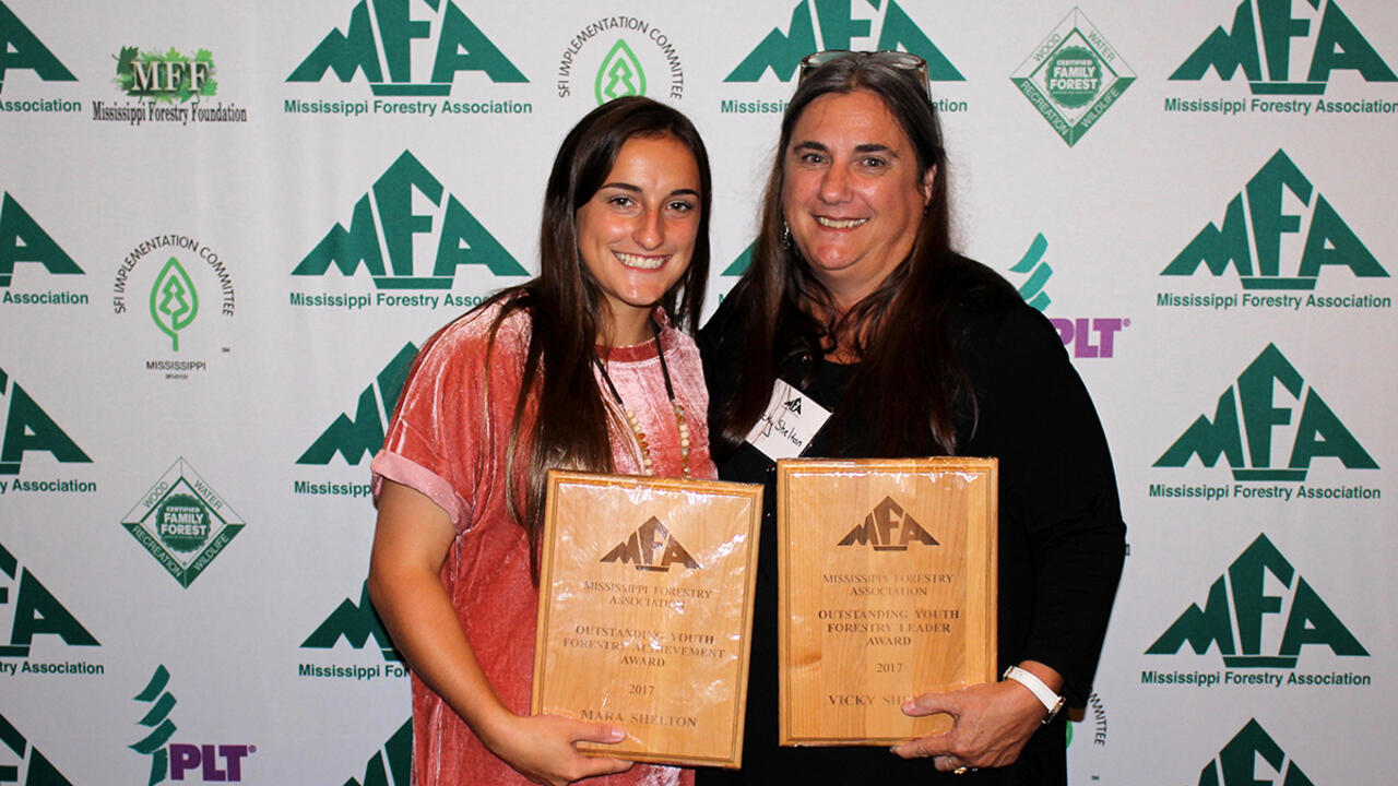 Two women stand while holding award plaques at the Mississippi Forestry Association annual meeting. 