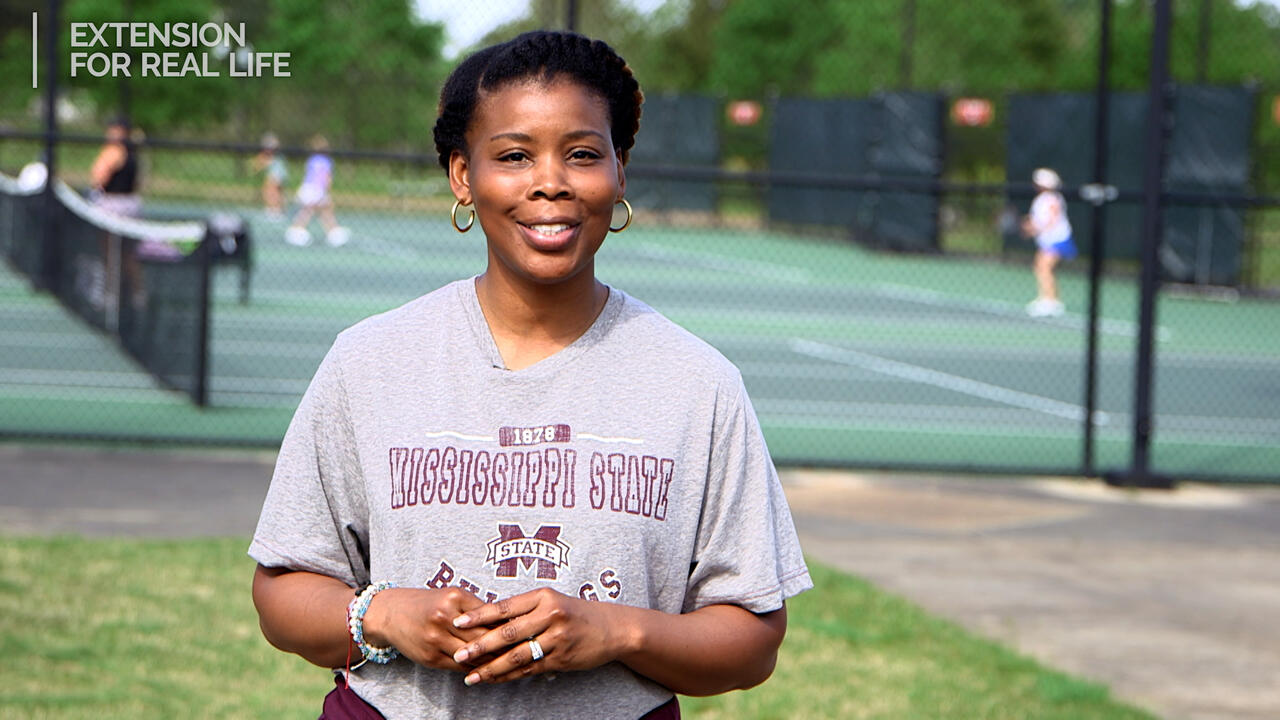 A woman stands in front of a tennis court