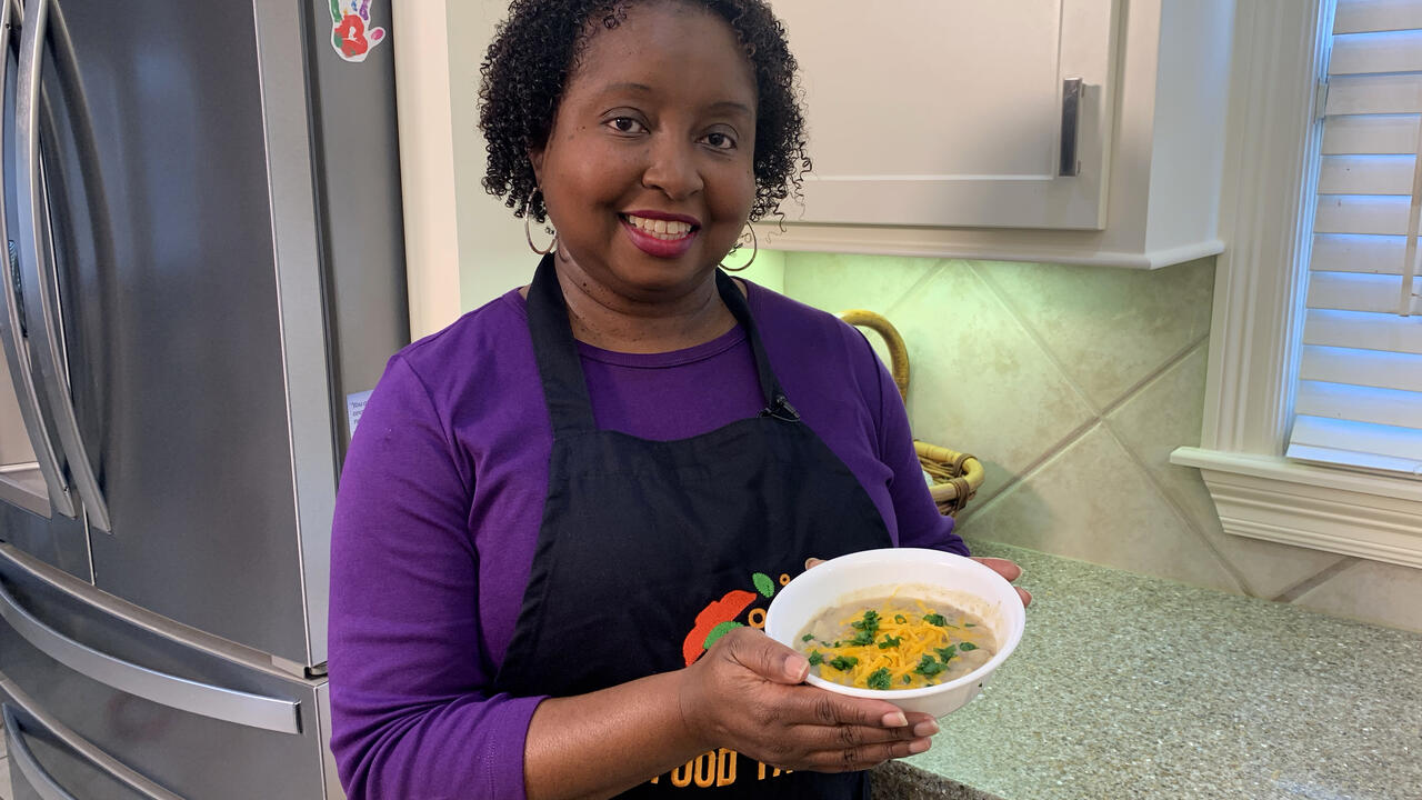 A woman holds up a bowl of Creamy Hamburger Potato Soup