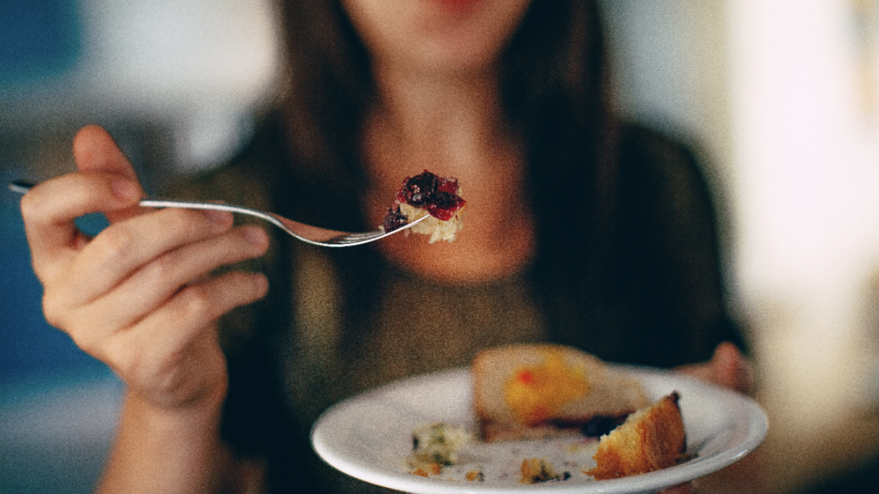 A person holding a fork and plate with food on it. 