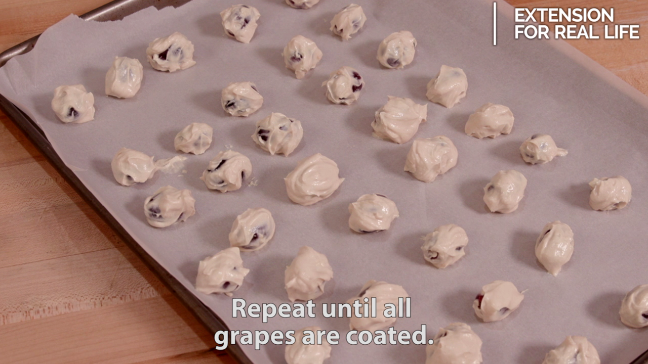 Red grapes dipped in a mixture of peanut butter and Greek yogurt lined up on a parchment paper covered baking sheet. 