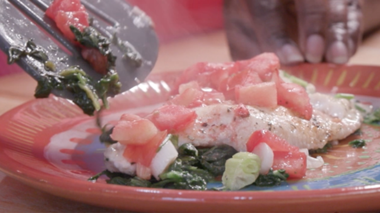 Baked fish with spinach, tomatoes, and onions sits on a plate.