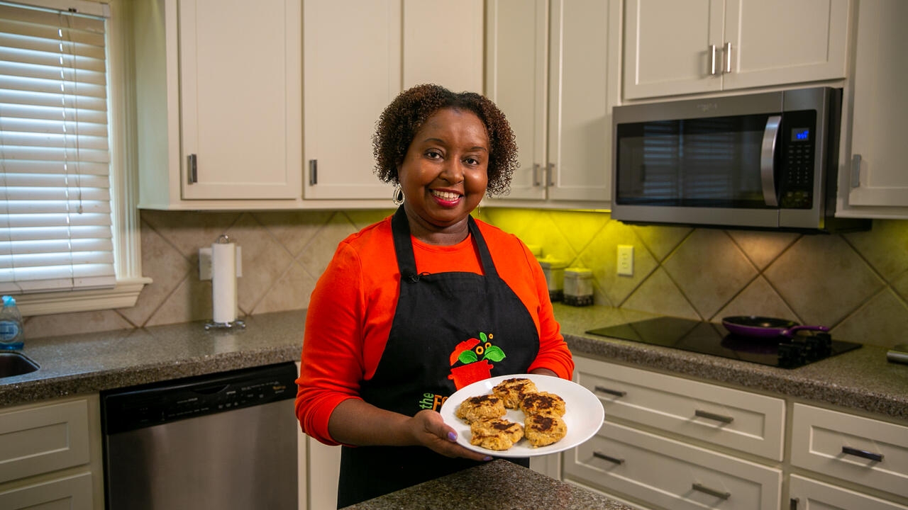 A woman stands in a kitchen holding a plate of salmon patties for the camera.