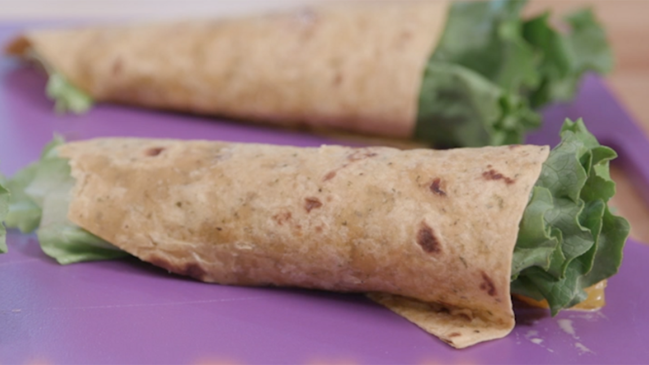  Green lettuce and cooked chicken wrapped in a wheat tortilla. 