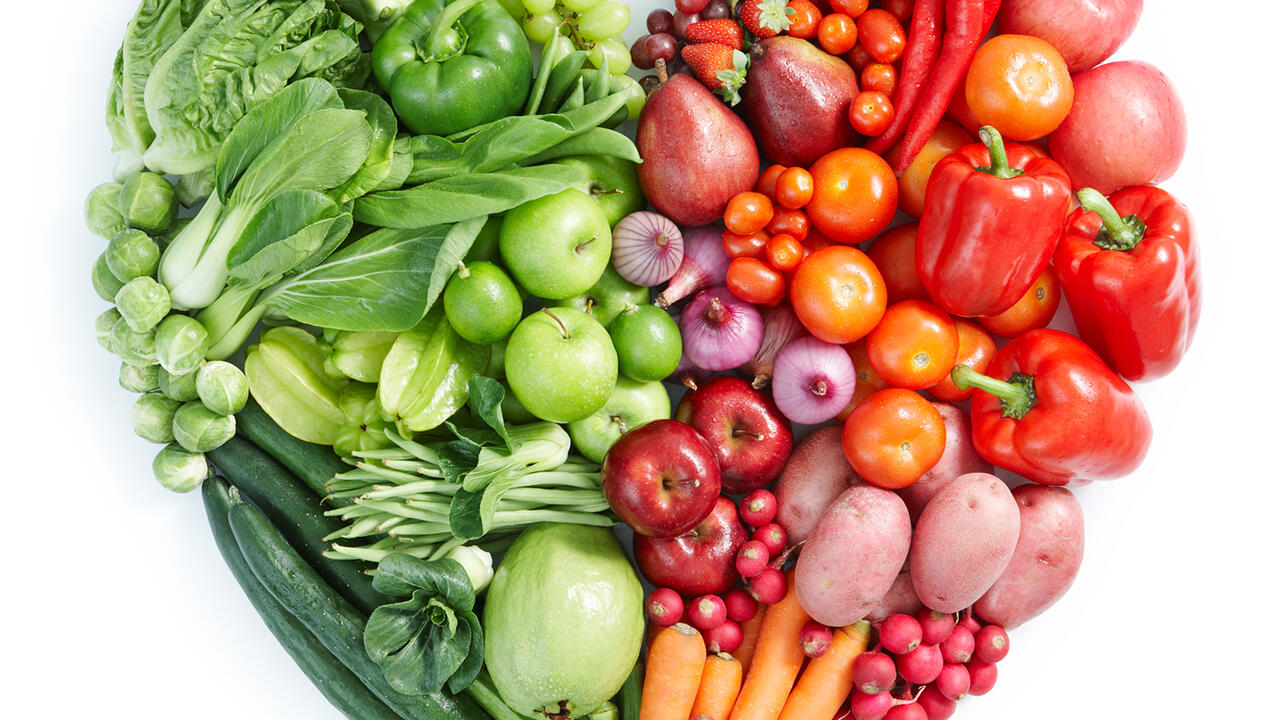 An assortment of green, orange, and red vegetables are arranged in a heart shape. 