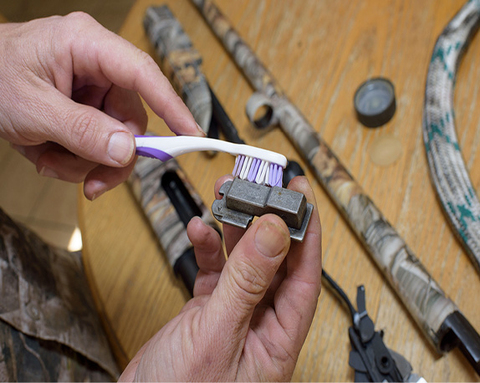 A clean, dry tooth brush is used to clean a gun part.