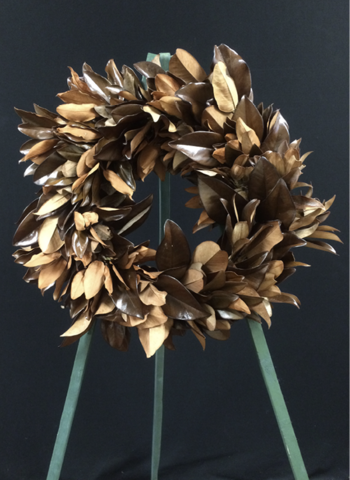 The finished preserved magnolia wreath on a wreath stand. It is simple and features some shiny and some matte brown leaves.