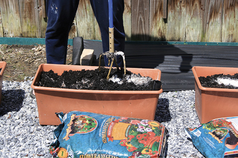 A person uses a garden claw to mix soil in a brown container.