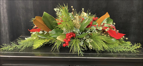 A christmas floral arrangement with various greenery and red berries.