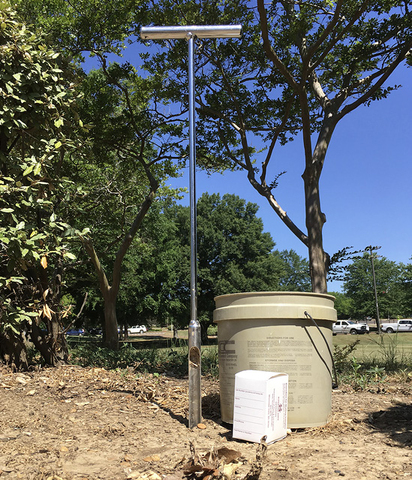 Outdoor scene with a large plastic bucket, soil sample container, and soil probe, which is a long, narrow, metal tool for inserting into the ground and extracting soil samples.