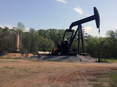 An oil rig on a raised drill pad, with bare dirt in the foreground and trees in the background.