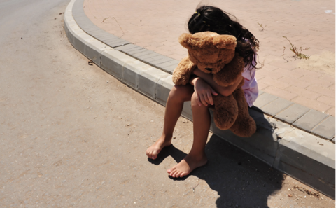 Young girl sitting on a curb hugging a large teddy bear.
