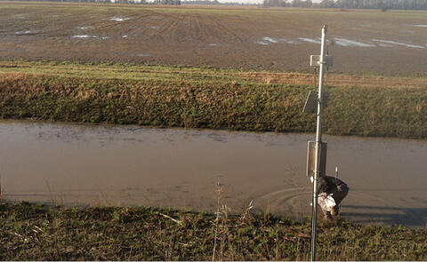 TWR ditch in spring (March). The ditch is full of water, and the surrounding field is brown and green.