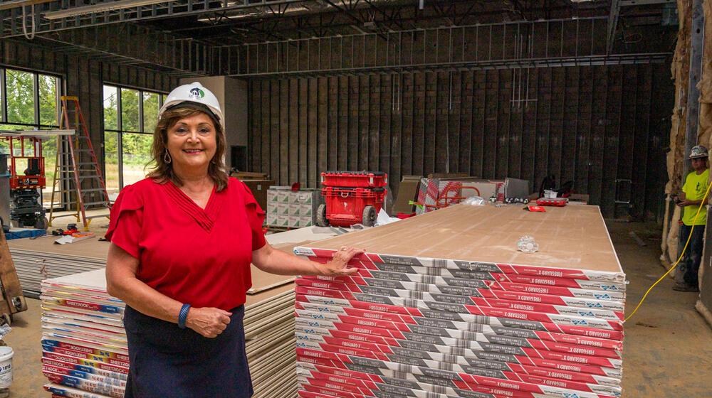A woman wearing a hard hat standing beside a stack of pallets.