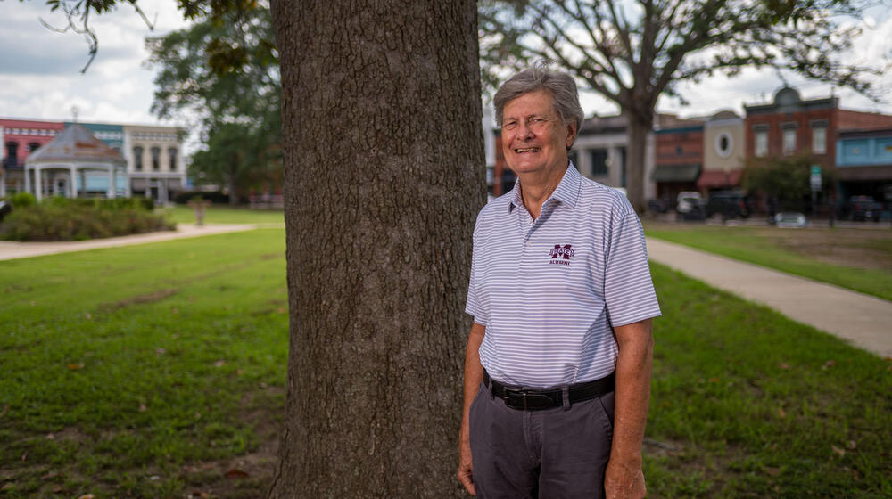 A man, wearing a Mississippi State University polo, smiling and standing in front of a tree.